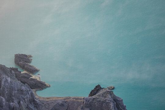 View of jagged rocks meet the opaque, milky turquoise waters, a scene where the earth's raw beauty unfolds in a symphony of color and texture, Ijen Volcano Crater, East Java, Indonesia.