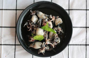 Stir fry squid in black squid ink sauce in black plate on table. Top view.