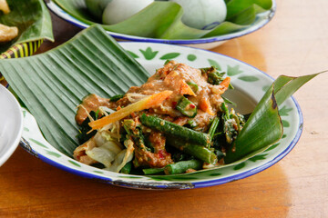 Indonesian vegetable salad with peanut sauce or pecel on vintage enamel plate  lined with banana leaves, places on ethnic fabric