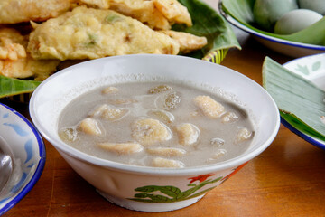 Kolak pisang, traditional Indonesian dessert made of bananas cooked in coconut milk and palm sugar syrup, served  in a white bowl. Setting appears to be a wooden table. 