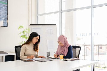 Attractive and friendly young Asian businesswoman training and giving an advice to her Muslim...
