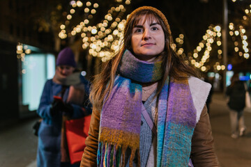 Adult woman walking down a Christmas decorated street at night.