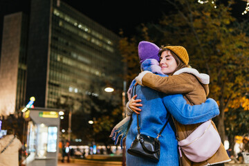 Women hugging at christmas market in city at night