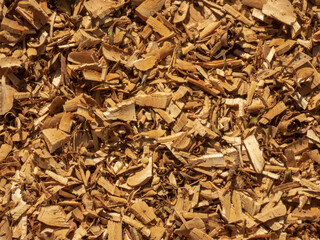 A close-up view of irregularly shaped wooden wood chips with varying shades of brown and tan,...