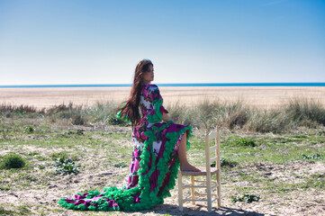 Woman dancing flamenco in white dress with floral print and ruffles, rests one bare foot on a...