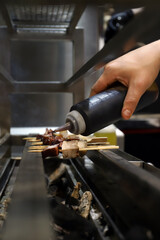 chef echando salsa a una brochetas de carne y pulpo que se están asando en un horno