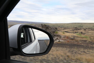 image of a gravel road in a rear view mirror with the icelandic volcanic landscape on the side of the car unsharp by movement