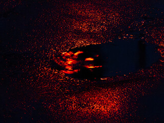 Colorful reflections on wet asphalt create a vibrant display during nighttime rain in an urban...