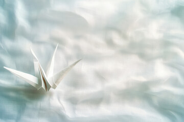 Paper crane sits on soft, textured fabric