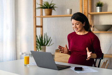 Pregnant woman having an online conference video call with her colleagues while working from home.