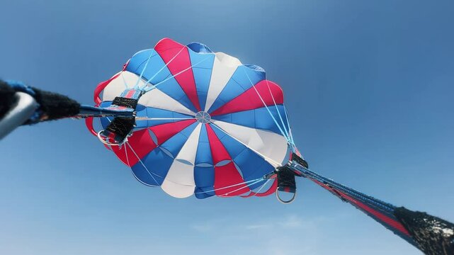 Exhilarating view of a vibrant red, white, and blue parasail hovering high against a clear blue sky