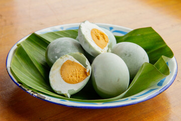 Salted duck eggs are displayed in a bowl lined with banana leaves. Two eggs are shown halved,...