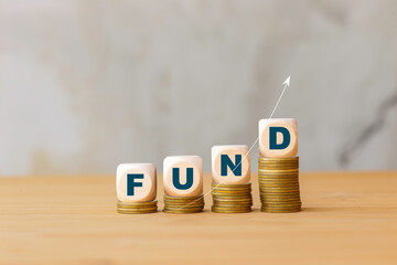 Stacks of coins topped with "FUND" blocks and an upward arrow, symbolizing increasing investment funds, financial growth, and successful fund management.