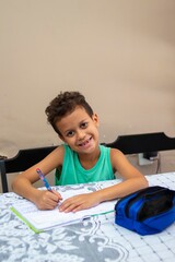 Young boy writing at a table, smiling.