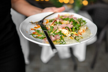 Gourmet dish on white plate with ham, arugula, cheese, and creamy sauce, garnished with orange...
