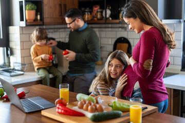 Pregnant mother, daughter tenderly embracing while father and son having fun at home during the day