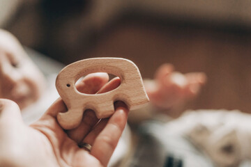 Infant extends hand toward a wooden elephant toy held nearby. The handcrafted toy captures the baby's attention, representing a moment of curiosity and early learning.
