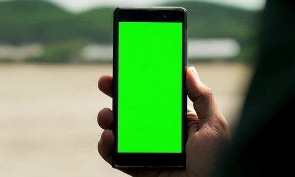 Close-up of a hand holding a smartphone with a green screen, ideal for mockups or visual effects in digital content and app design presentations