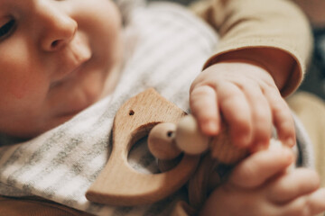 Close-up of a baby gnawing on a wooden teething toy, showcasing their curiosity and oral...
