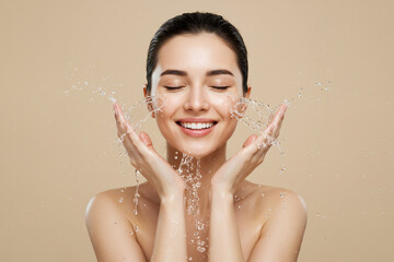 Young woman washing face with water splash on beige background, copy space