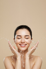Young woman washing face with water splash on beige background, copy space