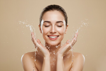 Young woman washing face with water splash on beige background, copy space