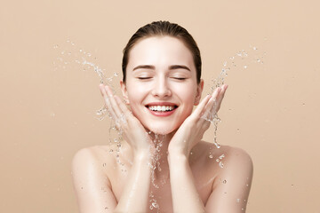 Young woman washing face with water splash on beige background, copy space