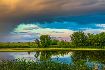 Rain clouds over the river with vegetation and trees on the banks. Scenic view of the landscape in a non-urban area