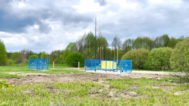 Industrial communication equipment installation surrounded by greenery, featuring a blue fenced area with yellow machinery and tall antennas, showcasing modern technology in a natural setting