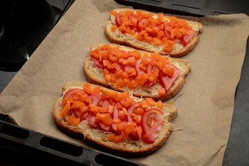 Close-up of tomato bruschetta on artisan bread slices with fresh sliced ​​tomatoes, parmesan cheese and herbs on a baking sheet in the oven while cooking. Food preparation process, bruschetta, sandwic