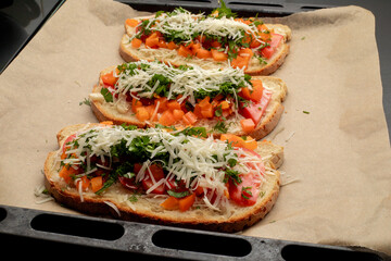 Close-up of tomato bruschetta on artisan bread slices with fresh sliced ​​tomatoes, parmesan cheese and herbs on a baking sheet in the oven while cooking. Food preparation process, bruschetta, sandwic