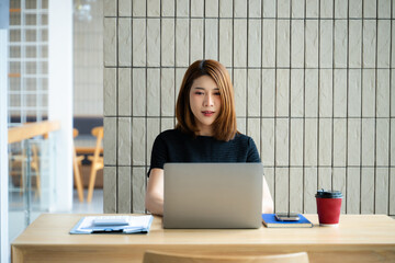 Asian businesswoman on smartphone while reviewing clipboard and laptop in a modern remote office.
