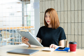 Asian businesswoman taps smartphone in a modern office workspace, highlighting digital...