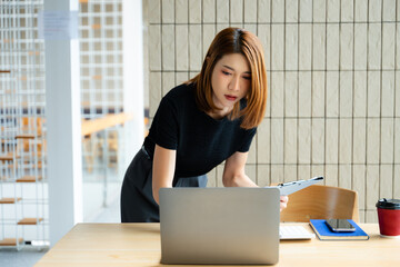 Asian businesswoman calculates finances on a clipboard with calculator by her laptop and smartphone...