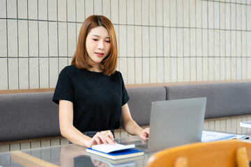 Asian businesswoman taps smartphone in a modern office workspace, highlighting digital...