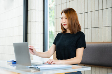 Asian businesswoman taps smartphone in a modern office workspace, highlighting digital...