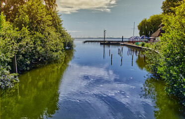 Calm river flows into lake with restaurant on shore and wind turbines in background on sunny summer...