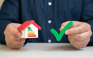 A man holds a green check mark near a house with an energy efficiency scale. Certificate of...