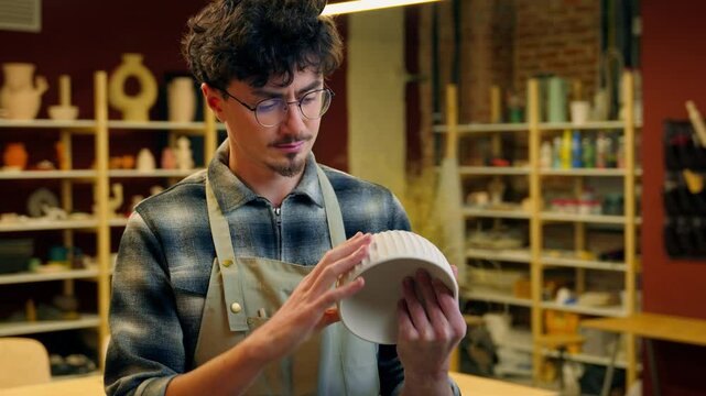 Caucasian man potter holding bowl handmade pottery stoneware product porcelain handcraft in workshop smiling male guy artisan sculptor craftsman designer small business owner showing ceramic art work