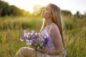 Beautiful woman with bouquet of wildflowers enjoying sunny day in meadow