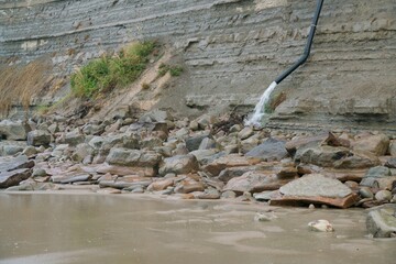 Water Flowing from Black Pipe on Coastal Cliff in Stormy Weather