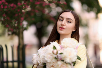 Woman with bouquet of beautiful peonies on city street. Space for text
