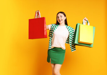 Positive woman with shopping bags on yellow background