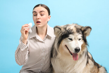 Woman suffering from allergy with her dog on light blue background
