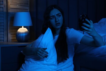Frustrated woman with pillow and alarm clock suffering from insomnia on floor at home