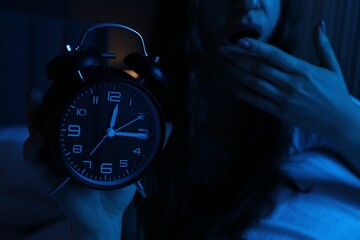 Frustrated woman with alarm clock suffering from insomnia on bed at home, closeup