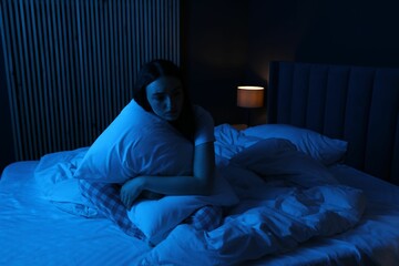 Frustrated woman with pillow suffering from insomnia on bed at home