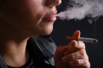 Woman smoking cigarette on black background, closeup