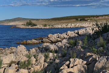 Summer landscape with rocky Croatian shoreline south of Razanac town, northern Dalmatia, Croatia. Bay water and arid foliage visible, blue skies in background. 