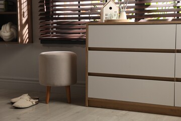Stylish pouf and slippers near chest of drawers at home